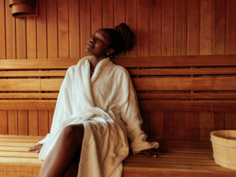 African American woman relaxing in a sauna wearing a robe. 